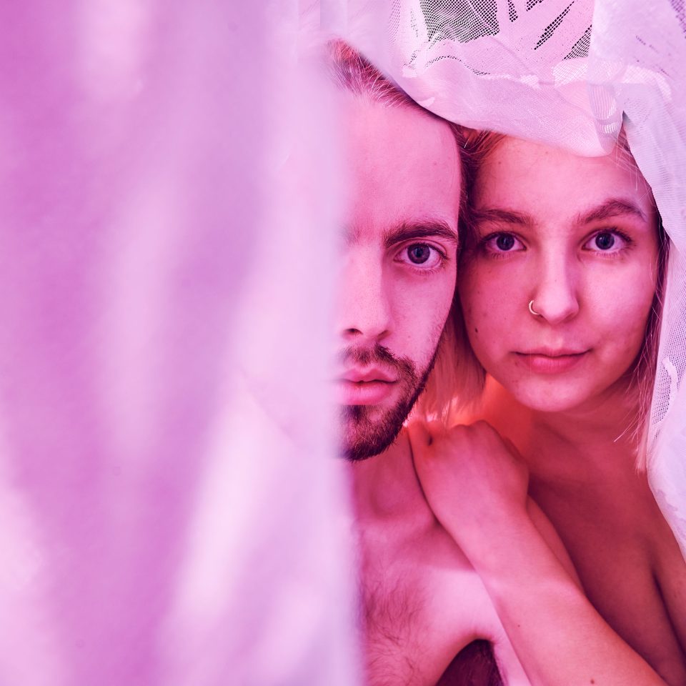 Emelie Zilliacus and Martin Paul look into the camera, surrounded by a sheer pink fabric.