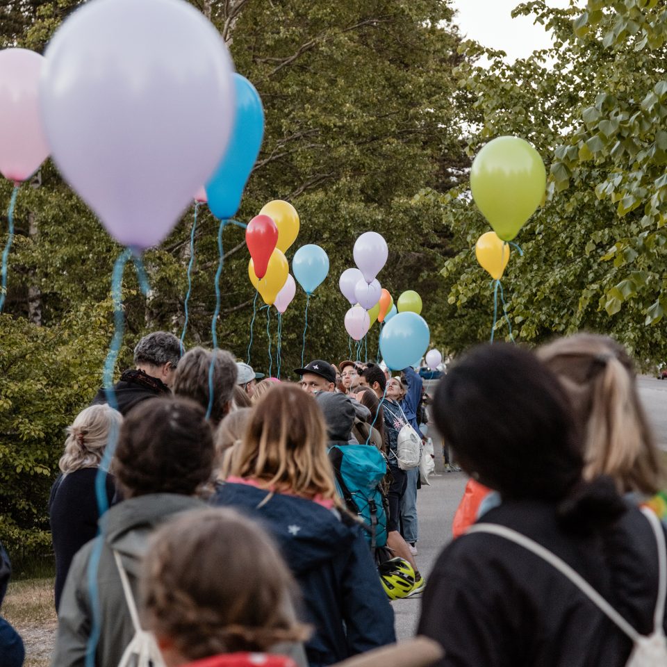 En stor grupp av människor går ute på gatan, många håller i ballonger.