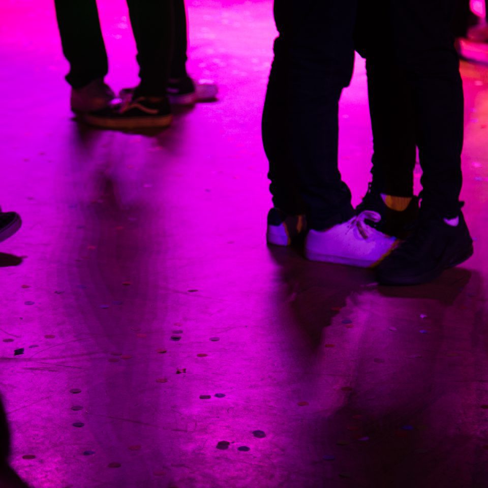 Personer på dansgolv, på bilden syns bara fötter nära varandra, ljusdesignen är pink.
