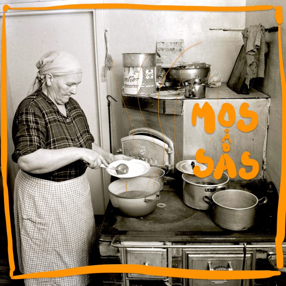 En äldre kvinna, klädd i gammaldags kläder, står framför spisen och sätter mat på en tallrik, svartvit bild.