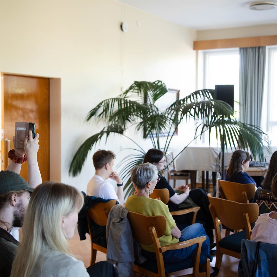 Publiken sitter på stolar i stadshusets foajé och lyssnar på en föreläsning.